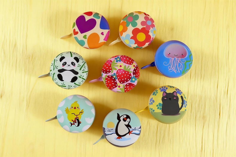 May include: Nine decorative bicycle bells with diverse patterns, such as hearts, flowers, and a panda. Other designs include strawberries, a cat, a penguin, and a chick. Each bell has a small lever.