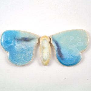 Op de afbeelding: Een keramische vlinder met blauwe en witte glazuur. De vlinder heeft een lichtgele body en is een decoratief stuk.