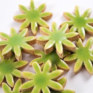 May include: A group of green and brown ceramic tile shaped like a flower with six points. The tiles are arranged in a random pattern.