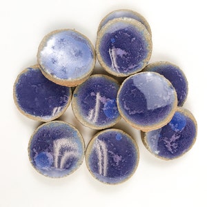 May include: A group of eight small, round ceramic dishes with a light blue glaze and a subtle white pattern. The dishes are arranged in a cluster on a white background.