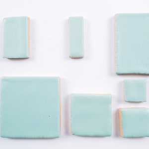 May include: A set of six light blue ceramic tiles in various sizes and shapes. The tiles have a smooth, matte finish.