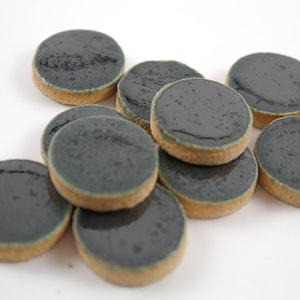 Può includere: Un gruppo di piastrelle di ceramica rotonde con una smaltatura verde scuro. Le piastrelle hanno una superficie leggermente strutturata e un bordo marrone chiaro.