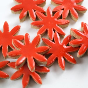 May include: A group of red and brown ceramic flower-shaped tiles. The tiles are arranged in a random pattern on a white background.