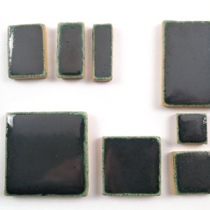May include: Assortment of dark green ceramic tiles with a light brown border. The tiles are in various sizes and shapes, including square and rectangular.