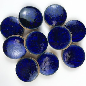 Könnte beinhalten: Zehn runde Keramikfliesen mit einer tiefblauen Glasur. Die Fliesen haben eine leicht unebene Oberfläche und einen hellbraunen Rand.