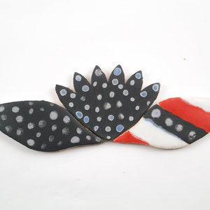 May include: Three ceramic tiles with a black, white, and red color scheme. The tiles are decorated with white and blue polka dots. The tiles are arranged in a flower shape.
