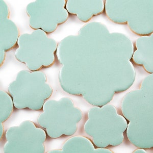 May include: A collection of light blue ceramic tiles in the shape of a flower. The tiles are arranged in a random pattern on a white background.