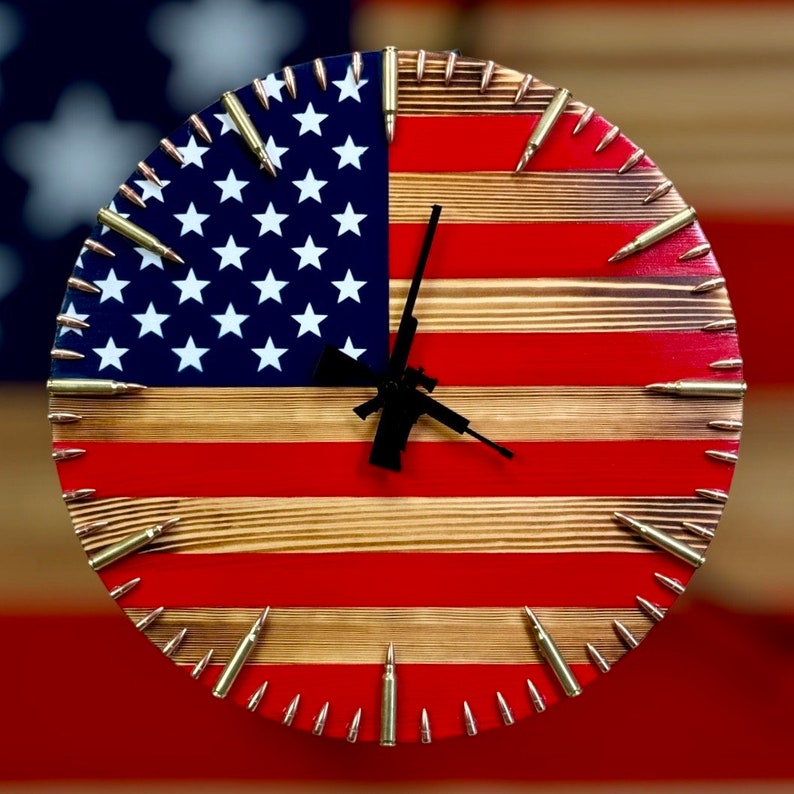 Peut inclure: Une horloge en bois avec un design de drapeau am&eacute;ricain rouge, blanc et bleu. Le cadran de l'horloge est entour&eacute; de douilles de balles.