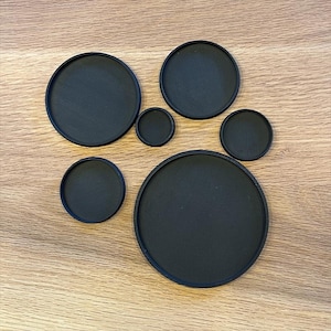 Könnte beinhalten: Satz mit sechs runden schwarzen Untersetzern in verschiedenen Größen. Die Untersetzer bestehen aus einem glatten, strukturierten Material.