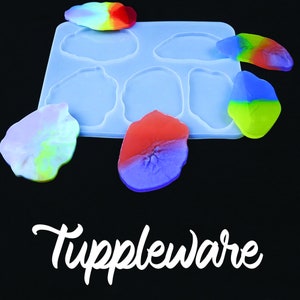 May include: A clear silicone mold with six irregular-shaped cavities, alongside several colorful resin pieces. The resin pieces are in shades of red, blue, yellow, and green. The word "Tuppleware" is written in white script at the bottom.