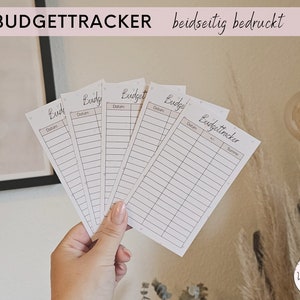 Könnte beinhalten: Fünf weiße Budget-Tracker-Karten mit dem Wort "Budget" auf jeder Karte. Die Karten haben eine Zeile für das Datum und eine Spalte für den Betrag. Die Karten sind beidseitig bedruckt. Die Karten liegen auf einem Tisch mit einer hellbraunen Oberfläche.
