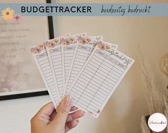 May include: Five white cards with floral designs and the text "Budgettracker" and "Datum" (German for "Date") printed on them. The cards are held in a hand.