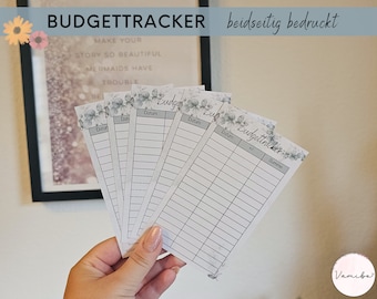 May include: Five white budget tracker cards with a floral design. The cards have a gray floral border and the words "Budgettracker" and "Summe" are printed on the cards. The cards are held in a hand.