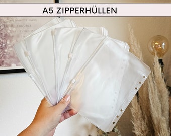 May include: A set of five clear plastic A5 zippered pouches with holes for a binder. The pouches are stacked on top of each other.