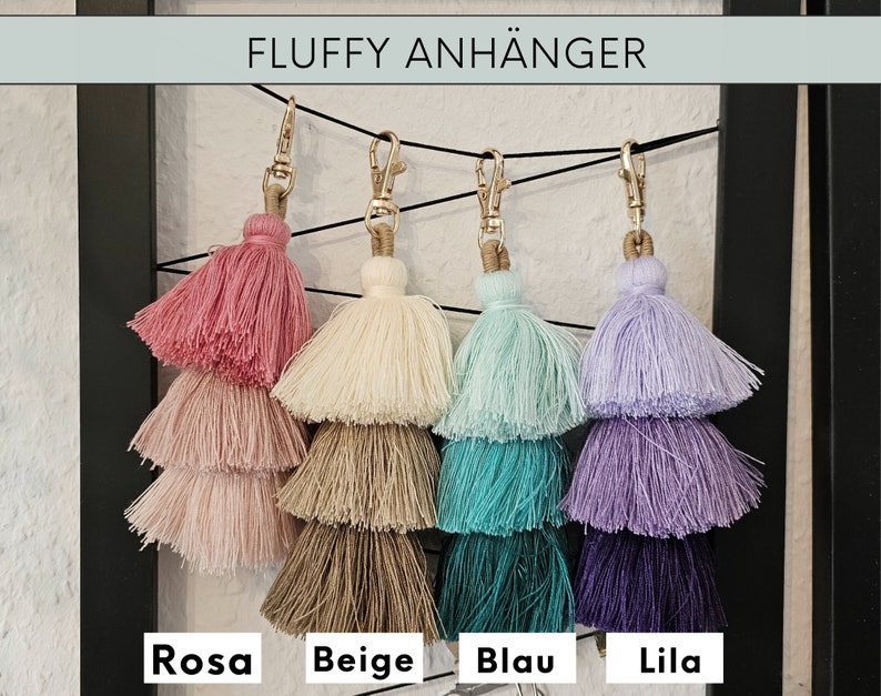 May include: Four fluffy tassel keychains in pink, beige, blue, and purple. The keychains are layered with three tassels each, and they are hanging from gold clasps. The text "FLUFFY ANH&Auml;NGER" is at the top of the image, and the colors are labeled "Rosa", "Beige", "Blau", and "Lila" at the bottom.