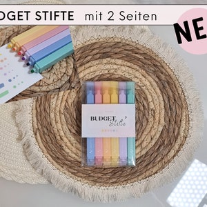 Könnte beinhalten: Ein Set pastellfarbener Textmarker mit dem Text "BUDGET STIFTE" und "mit 2 Seiten" auf der Verpackung. Die Textmarker sind auf einem gewebten Platzset angeordnet, mit einer Farbmusterkarte. Das Wort "NEU" befindet sich in einem rosa Kreis.