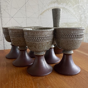 May include: A collection of six ceramic goblets and a small vase. The goblets feature a speckled, light brown bowl with a decorative band, resting on a dark brown pedestal base. The vase is a similar speckled brown colour.