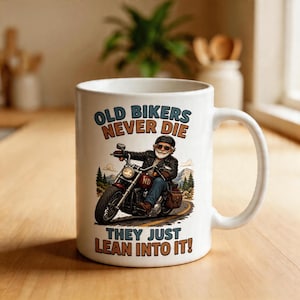 May include: White ceramic mug with a humorous graphic of an older biker riding a motorcycle. The mug features the text "OLD BIKERS NEVER DIE THEY JUST LEAN INTO IT!" in a vintage style.
