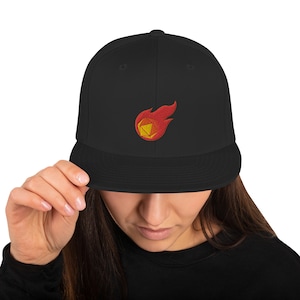 May include: Black fitted baseball cap with an embroidered design of a red and yellow flaming dice.