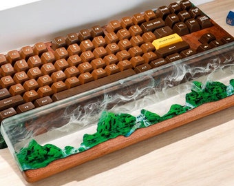 Puede incluir: Un reposamuñecas de madera para teclado con una parte superior de resina transparente que presenta un diseño de paisaje verde y blanco. El teclado es marrón con teclas amarillas y una tecla "SPACE BAR" blanca.