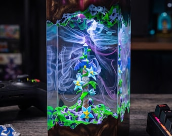May include: A rectangular resin lamp featuring a central pillar with blue flowers and green vines encased in clear material. The top and bottom sections are dark brown with textured green accents, and wispy white smoke effects are visible inside.