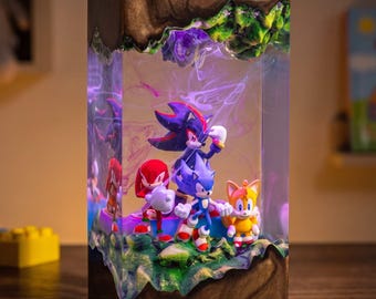 May include: A rectangular resin lamp featuring miniature figures of Shadow, Sonic, Knuckles, and Tails encased in clear material. The top and bottom sections are dark brown wood with green accents, and the interior glows with purple LED light.