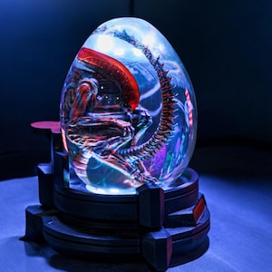 May include: A clear glass sphere with a glowing red and black alien creature inside. The sphere is on a black base with a silver ring around the top.