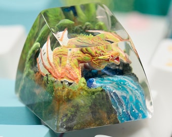 May include: A clear resin keycap with a miniature dragon and a waterfall scene inside. The dragon is orange, yellow, and red, and the waterfall is blue and white.