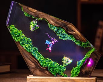 May include: A trapezoidal resin and wood lamp featuring a dark wood frame with embedded bright green moss-like textures. A small figure in a blue and red outfit is suspended in the center, illuminated by a purple light source from the base.