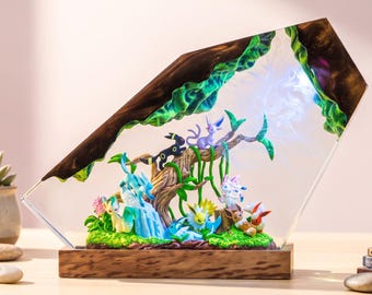 Puede incluir: Una lámpara decorativa de resina que presenta una colección de pequeñas figuras de criaturas coloridas dispuestas alrededor de una estructura de árbol central. La escena está encerrada en un bloque de resina transparente con base de madera.