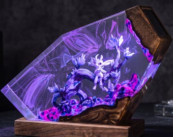 Puede incluir: Una lámpara decorativa con una pequeña criatura blanca sentada sobre una rama de madera oscura, encapsulada en un bloque de resina transparente. La resina contiene efectos de luz violeta y azul, con una base de madera maciza y un detalle superior.