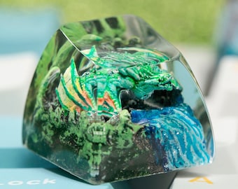 May include: A green dragon figurine encased in clear resin with a blue waterfall and green foliage. The resin piece is a keycap for a mechanical keyboard.