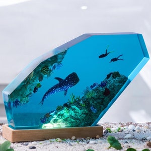 May include: A blue resin sculpture of an ocean scene with a whale shark, coral, and scuba divers. The sculpture is on a wooden base.