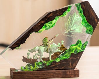 May include: A decorative resin and wood sculpture featuring a figure riding a white wolf, accompanied by small white spirits. The scene is encased in a clear, angular resin block with dark wood edges and vibrant green, swirling accents on a base.