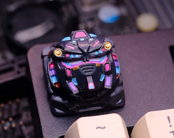 May include: A black and blue keyboard keycap with a colorful robot design. The keycap has a gold accent and is surrounded by other keyboard keys.