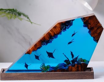 Puede incluir: Una escultura de resina que representa una escena de océano azul con mantarrayas y corales. La escultura está montada sobre una base de madera.