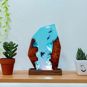 Könnte beinhalten: Eine blaue Harzskulptur mit einem Holzsockel, die eine Szene von Fischen zeigt, die im Meer schwimmen. Die Skulptur wird von innen beleuchtet und erzeugt so einen leuchtenden Effekt.