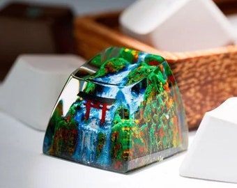 May include: A clear resin keycap with a colorful image of a waterfall and a red torii gate. The keycap is a vibrant green, blue, and red.
