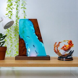 May include: A unique resin lamp with a blue river design, featuring miniature divers and fish. The lamp is set in a wooden frame and base. A colorful Charmander figurine is also on display.