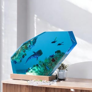 May include: A blue resin sculpture of an underwater scene with a whale shark, coral, and scuba divers. The sculpture is on a wooden base.