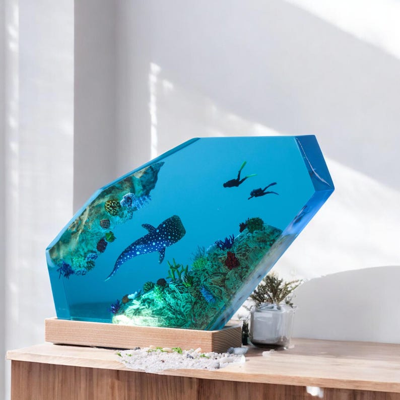 May include: A blue resin sculpture of an underwater scene with a whale shark, coral, and scuba divers. The sculpture is on a wooden base.