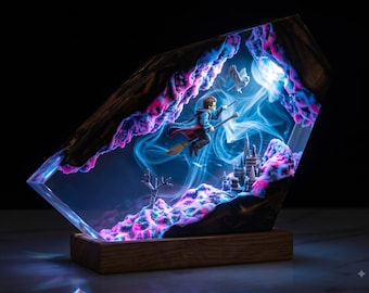 May include: A rectangular resin lamp featuring a miniature figure riding a broomstick, a small owl, and a castle structure. The interior glows with blue and pink light, surrounded by dark wood edges, all mounted on a solid wooden base.