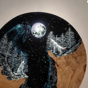 Puede incluir: Obra de arte redonda de madera que representa una escena nocturna con dos lobos blancos aullando a la luna llena. El fondo es azul oscuro con estrellas blancas y &aacute;rboles blancos estilizados. La parte inferior tiene un patr&oacute;n de vetas de madera.