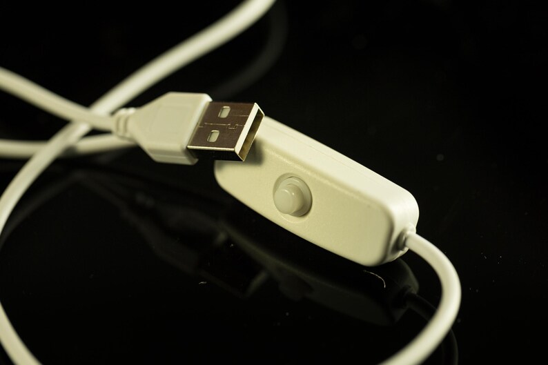 May include: Close-up of a white USB cable with a USB connector and an inline on/off switch. The cable and switch are against a black background, with the cable slightly out of focus.