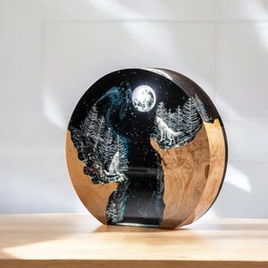Puede incluir: Escultura redonda y decorativa que representa una escena nocturna de bosque con dos lobos aullando a la luna. La escultura est&aacute; hecha de madera y resina, con un fondo negro y detalles blancos. Los lobos son plateados.