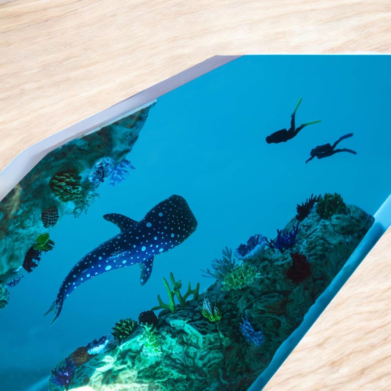 May include: A resin art piece depicting a whale shark swimming in a blue ocean with coral reefs and two scuba divers in the background.