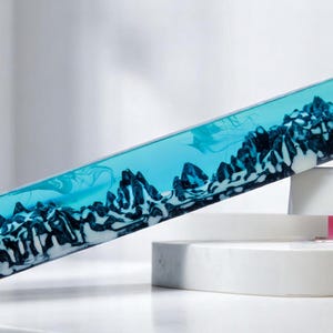 May include: A clear blue cylinder with a swirling black and white design inside. The cylinder is resting on a white surface.