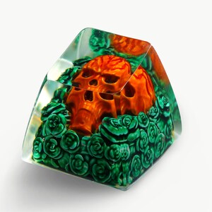 May include: A clear resin keycap with a detailed orange skull surrounded by green roses.