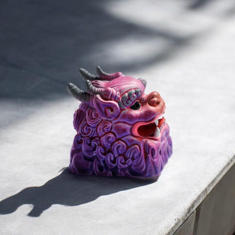 Pu&ograve; includere: Una statuetta in ceramica di colore viola e rosa che rappresenta una creatura mitologica con un'espressione feroce. La statuetta presenta dettagli intricati e una superficie testurizzata.
