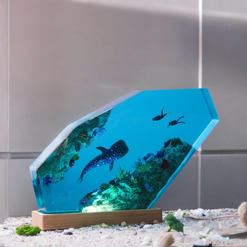 May include: A blue resin sculpture of a whale shark swimming in a coral reef. The sculpture is shaped like a diamond and has a wooden base.